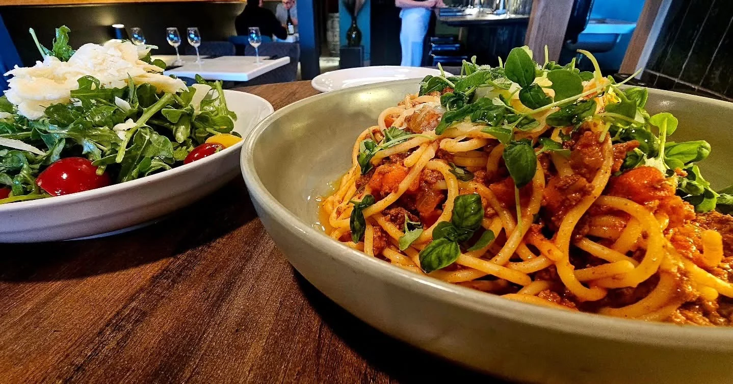Pasta topped with greens beside a salad in Trio’s dining room